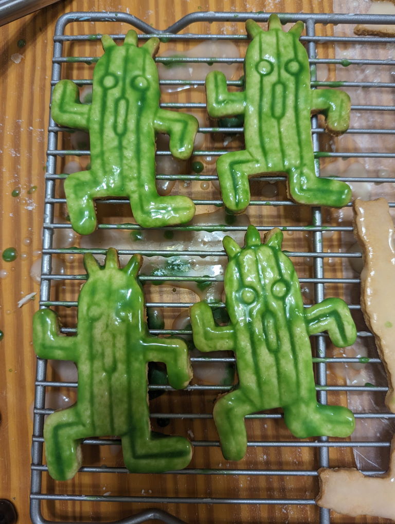 Four Cactuar sugar cookies covered in a blotchy, semi-transparent green icing. They look like they are decaying. It looks really sticky.